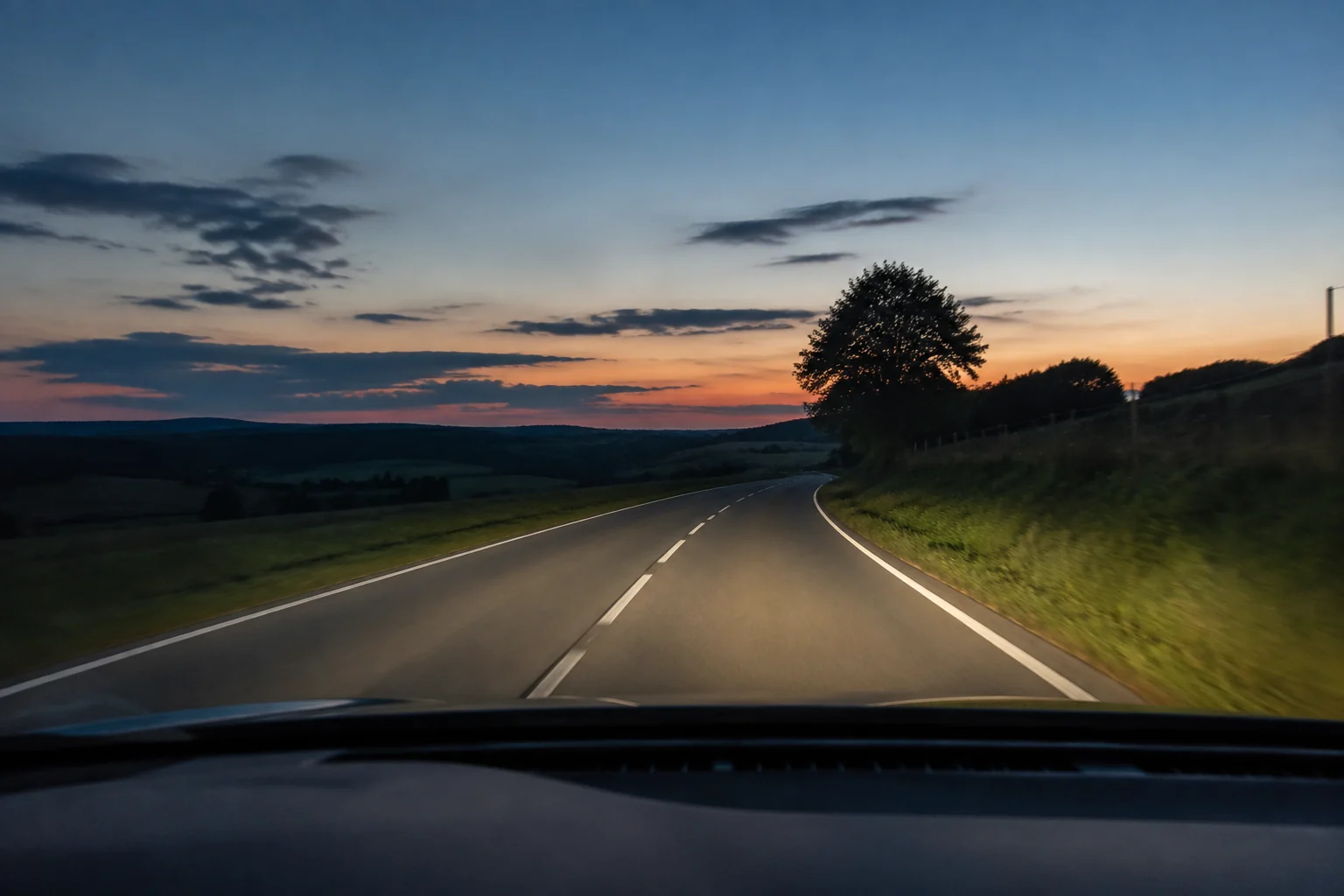 Route wallonne éclairée par les phares au crépuscule